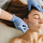 Closeup portrait beautiful woman during cosmetology procedures, rejuvenation in beauty salon. Dermatology procedure , painting eyebrows, hands in blue glows, at work, healthcare, botox.