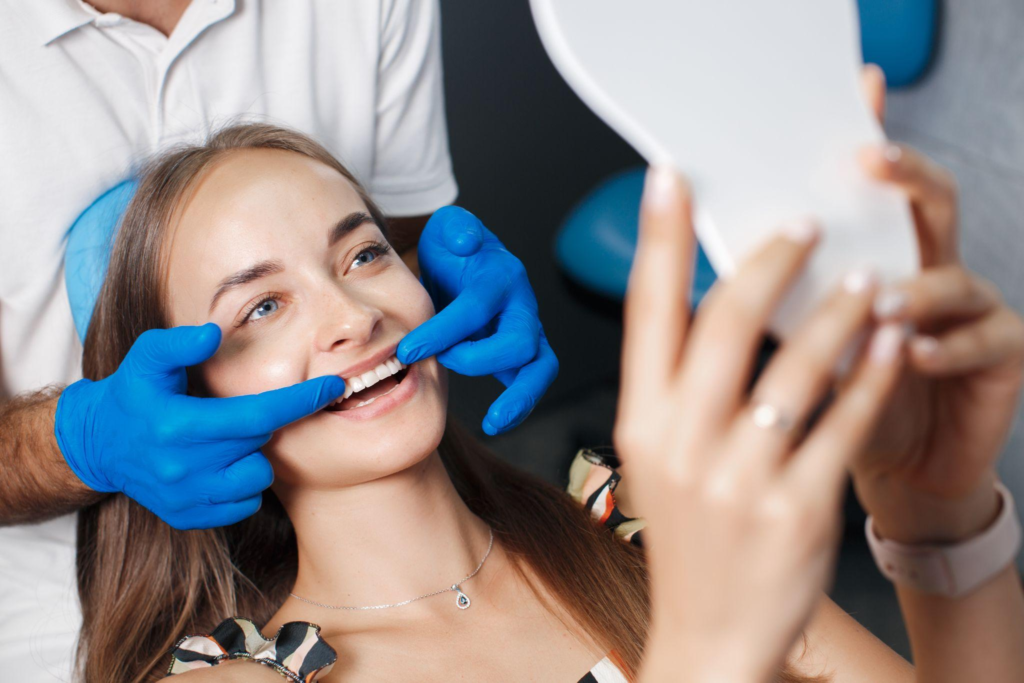 A woman smiling in the mirror as the dentist completes the veneer treatment 