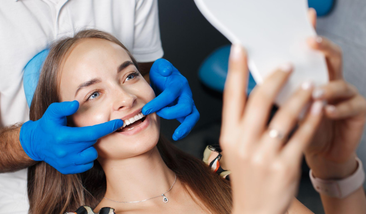 A woman smiling in the mirror as the dentist completes the veneer treatment