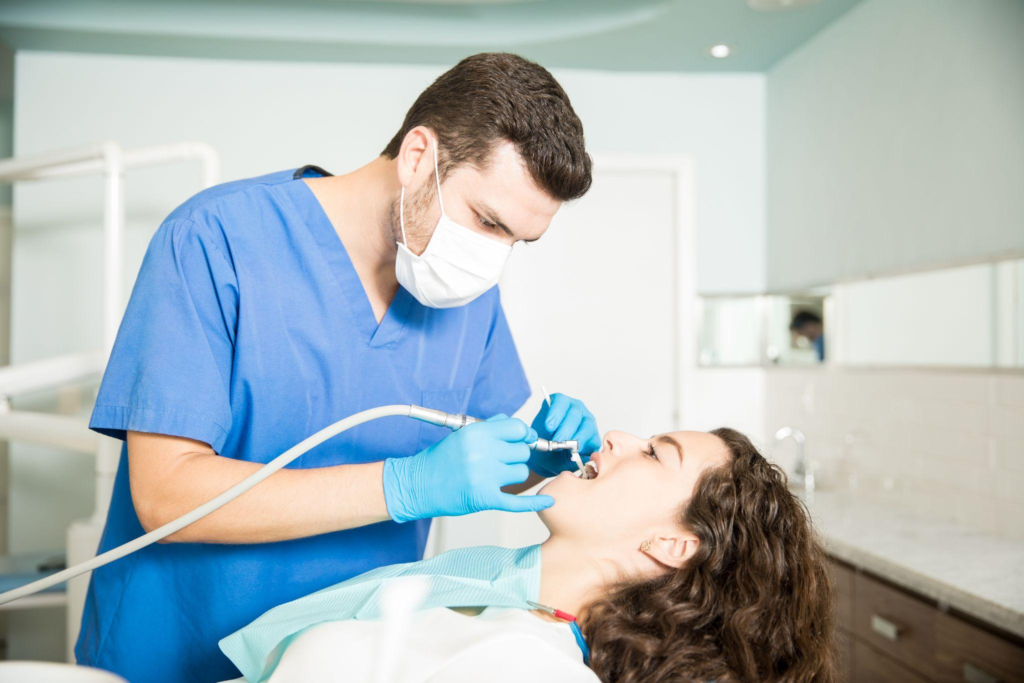 A woman undergoing a dental treatment while the dentist in blue scrubs provides the treatment