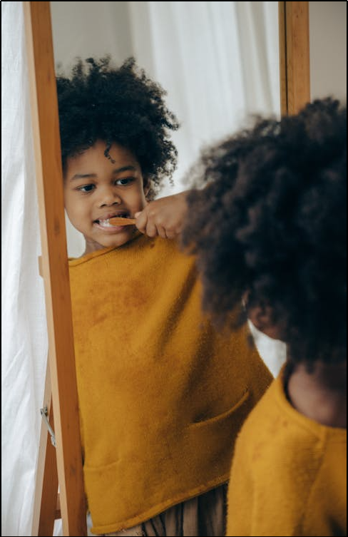 Cheerful boy brushing teeth against mirror-