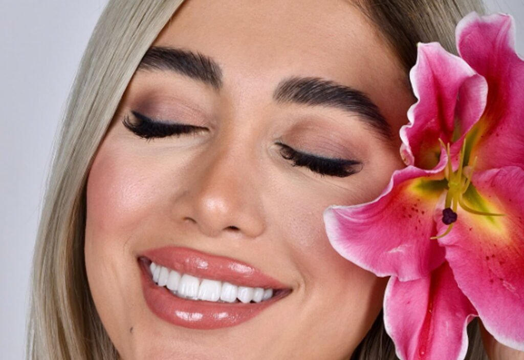 Woman smiling confidently with straight teeth after clear aligner treatment in Dubai, holding a pink lily flower.