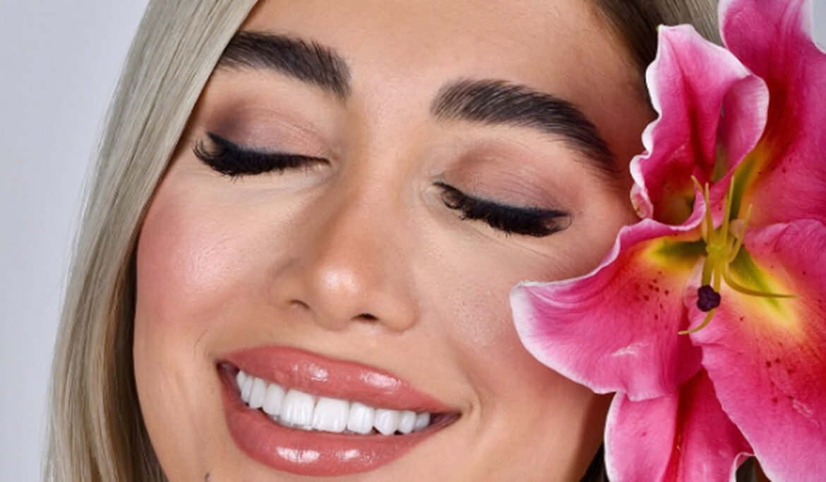 Woman smiling confidently with straight teeth after clear aligner treatment in Dubai, holding a pink lily flower.