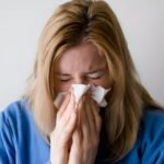 Woman sneezing into tissue suffering from seasonal allergy symptoms